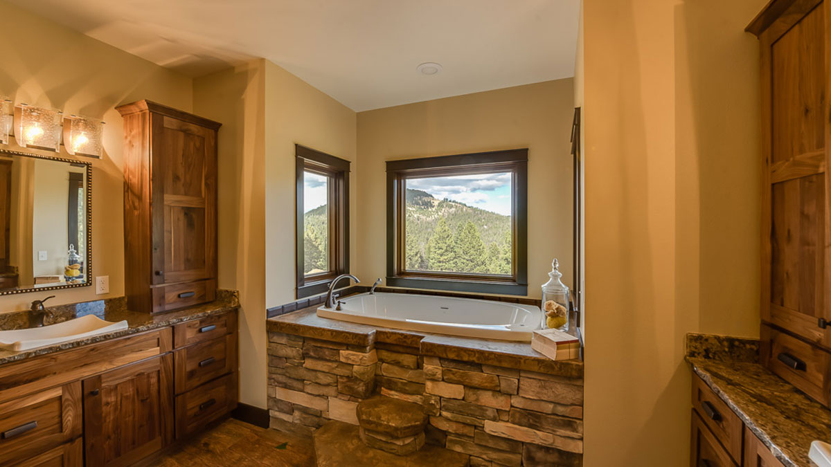 A large bathtub in a corner of the bathroom with granite around the top and rock steps up to it, with a view of a mountain