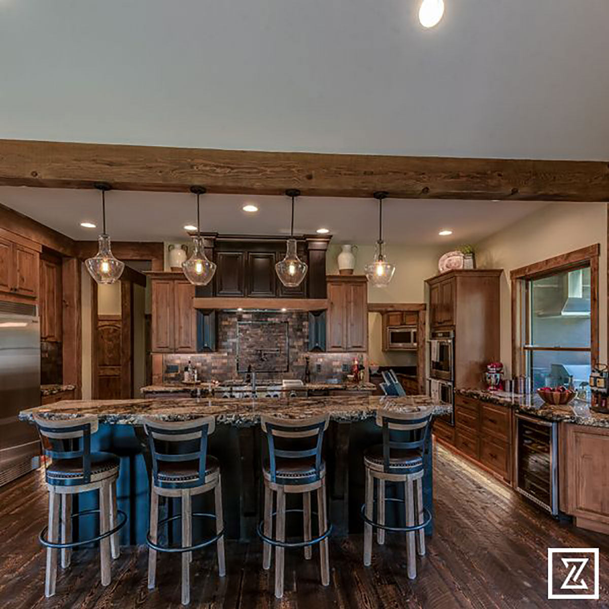 Distant view of kitchen with lights hanging over the bar in the center and you see a window and wine cooler off to the right