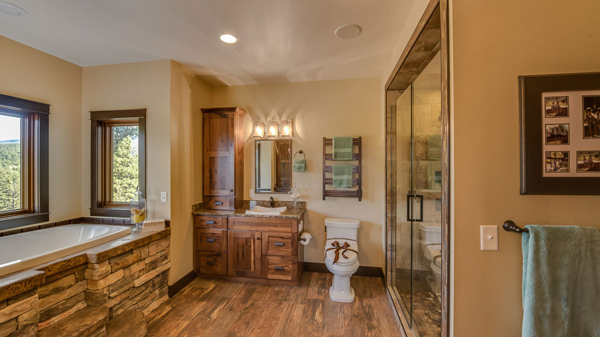 Bathtub off to the side with rock steps with a vanity in the center and a toilet with a bow on it next to a walk in shower