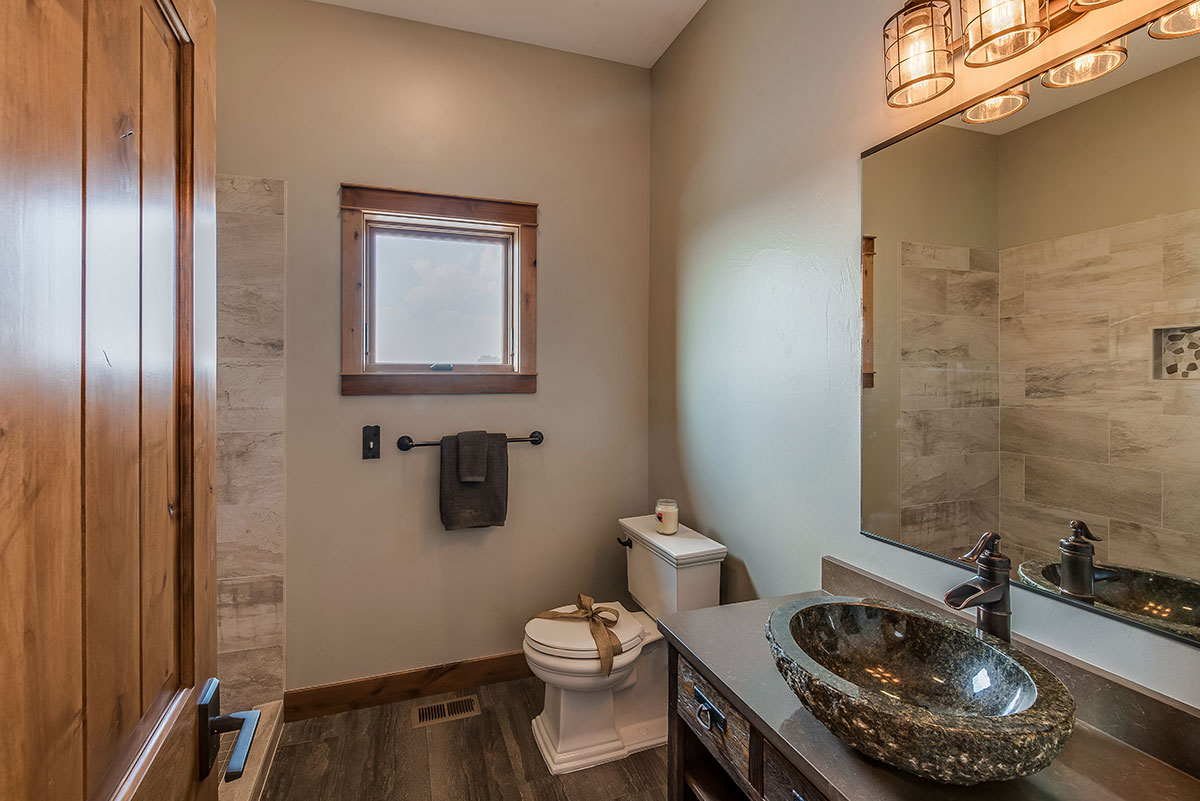 Guest bathroom with rustic cabinet with a granite top and carved rock sink next to a toilet with a bow on it