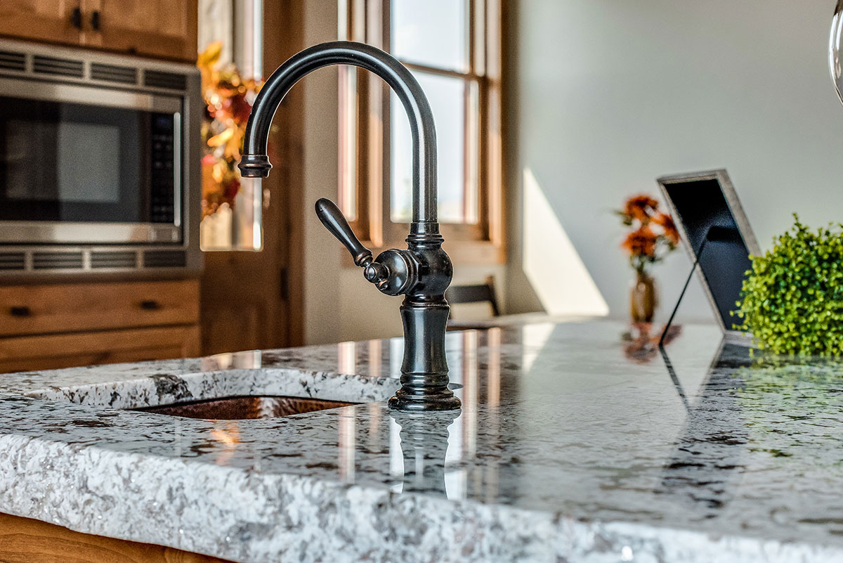 A close up of a raw granite countertop with a focus on a rubbed bronze faucet over a copper sink