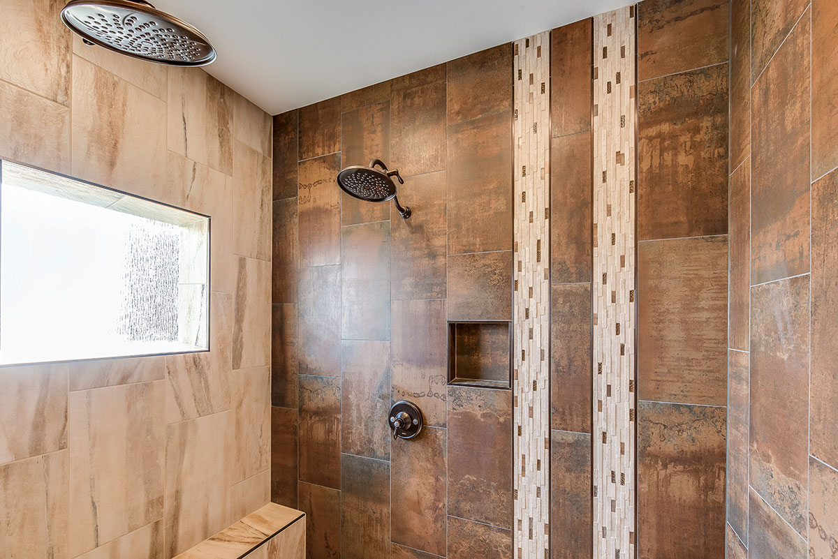 Large open shower with seat with frosted glass window against intricate tile work and shower head on the wall and ceiling