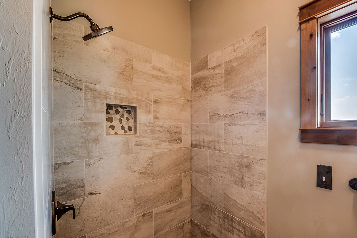 A custom shower with tile backsplash and bronze handle and showerhead with a window off to the right