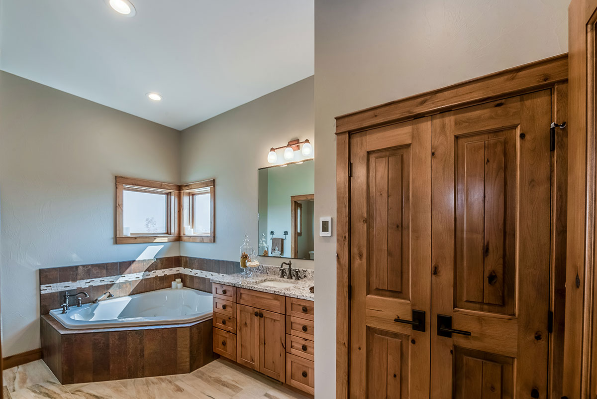 A large jacuzzi bathtub in the corner near a window and a vanity with a large closet in the foreground